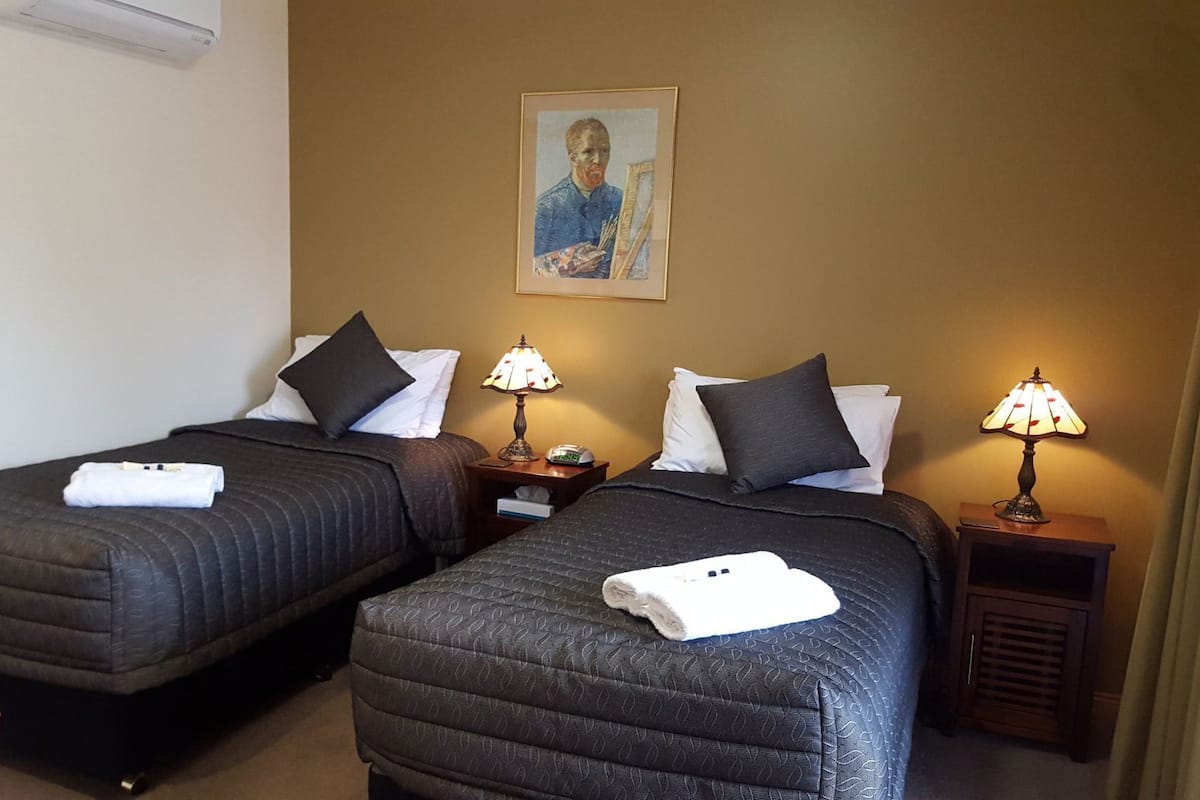 Habitación de hotel con dos camas, mesitas de noche con lámparas, un cuadro en la pared y un jarrón con tulipanes.