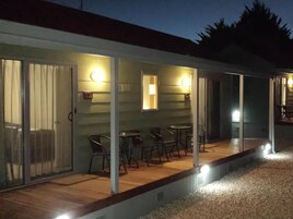 Un área de estar al aire libre con techado, mesas y sillas, una terraza de madera y un sendero de grava.