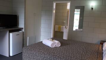 Habitación de hotel con cama, televisor, un refrigerador pequeño y un baño visible a través de una puerta abierta.