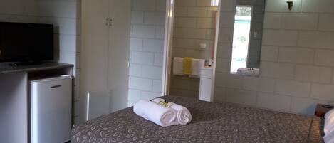 Habitación de hotel con cama, televisor, un refrigerador pequeño y un baño visible a través de una puerta abierta.
