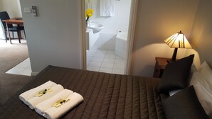 A hotel room with a bed, a bedside lamp, a bathroom visible through an open door, and a small table with a chair. - Daylesford Central Motor Inn (Daylesford)