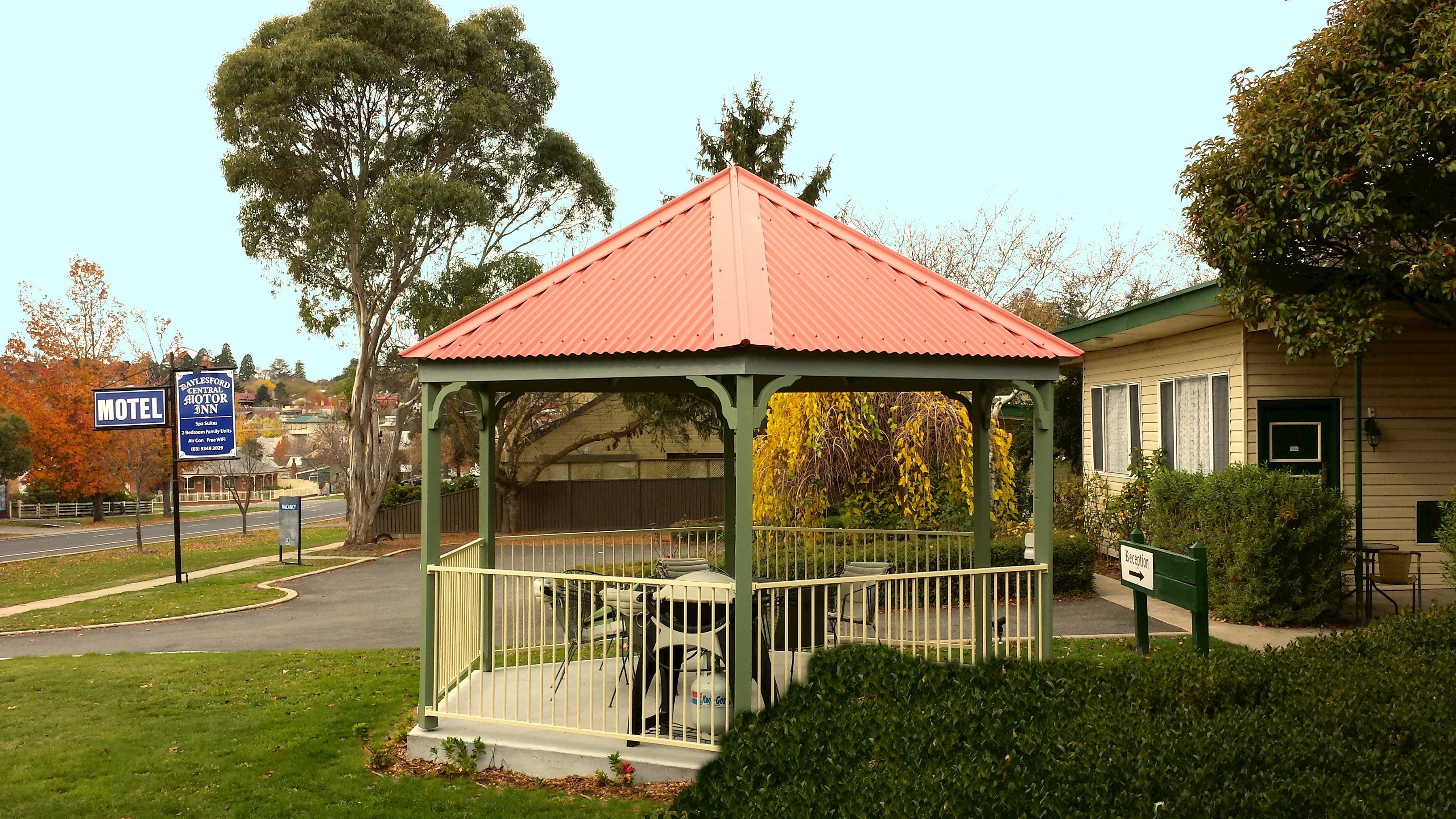 A gazebo with a red roof, surrounded by greenery and a motel sign in the background.