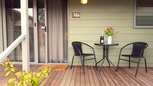 A wooden deck with two black wicker chairs and a small round table. A bottle of champagne and two glasses are on the table. A sign with the number 16A is visible on the wall. - Daylesford Central Motor Inn (Daylesford)