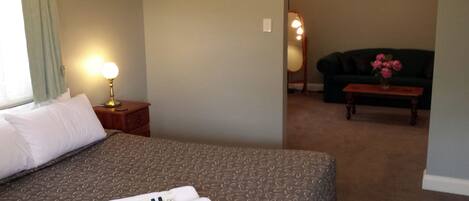 A hotel room with a bed, a bedside lamp, a nightstand, a green sofa, and a small table with a vase of flowers.