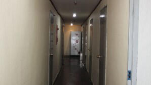 A narrow hallway with doors on both sides, leading to a room with a refrigerator. - Dongdaemun Guest House (Seoul)