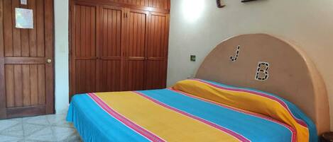 A bedroom with a bed, a wooden wardrobe, and a wall with a crescent moon and sun decoration.