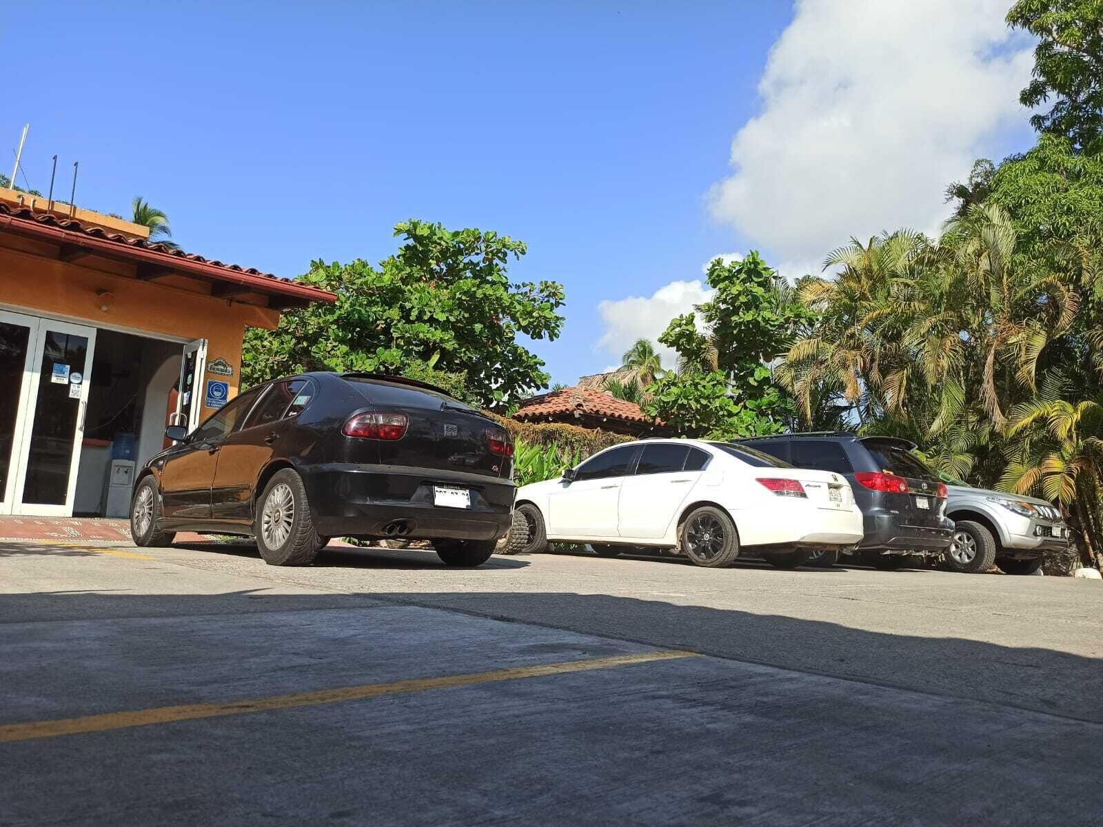 A parking area with three cars parked in front of a building with a red roof and a signboard.