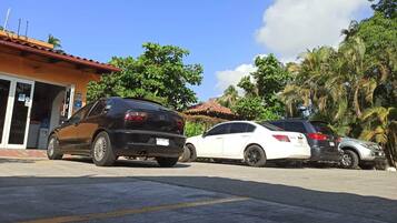 A parking area with three cars parked in front of a building with a red roof and a signboard.
