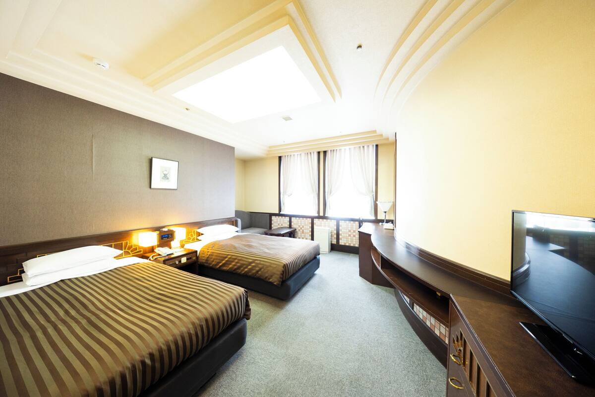 Une chambre d’hôtel avec deux lits, un téléviseur à écran plat, un bureau et une grande fenêtre avec des rideaux.