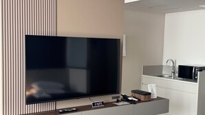 A modern living room with a large flat-screen TV, a small clock, and a remote control on a wooden console.