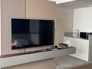 A modern living room with a large flat-screen TV, a small clock, and a remote control on a wooden console.