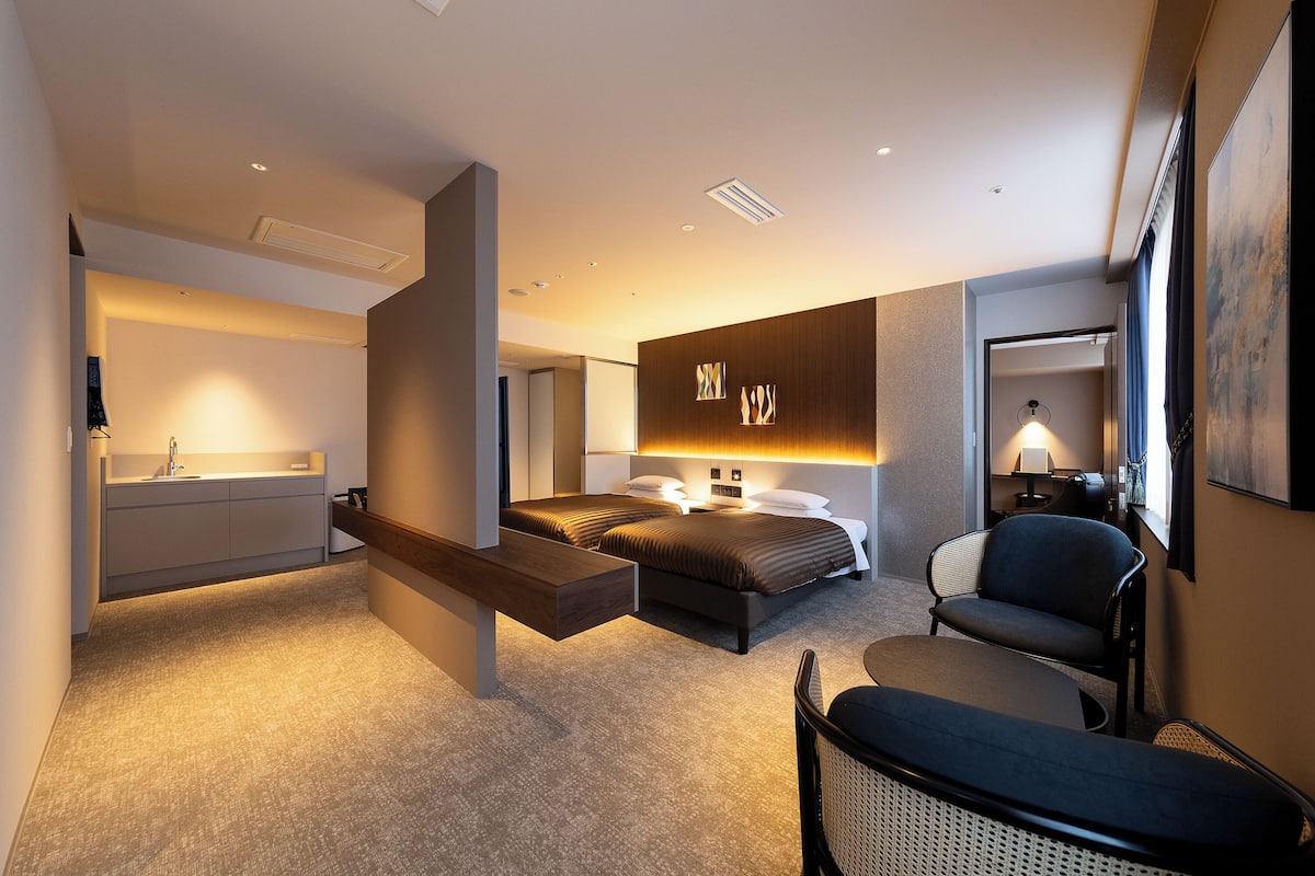 Une chambre d’hôtel moderne équipée d’un lit, d’une table de chevet, d’une chaise et d’un bureau avec une lampe.
