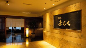 A hotel lobby with a reception desk, a large potted plant, and a sign with Japanese characters.