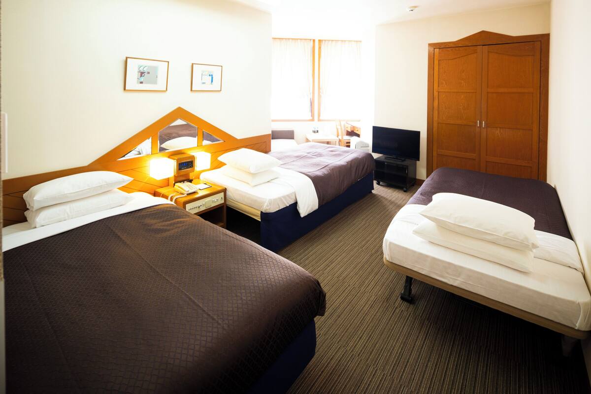 Une chambre d’hôtel avec deux lits, un bureau, une télévision et une armoire.
