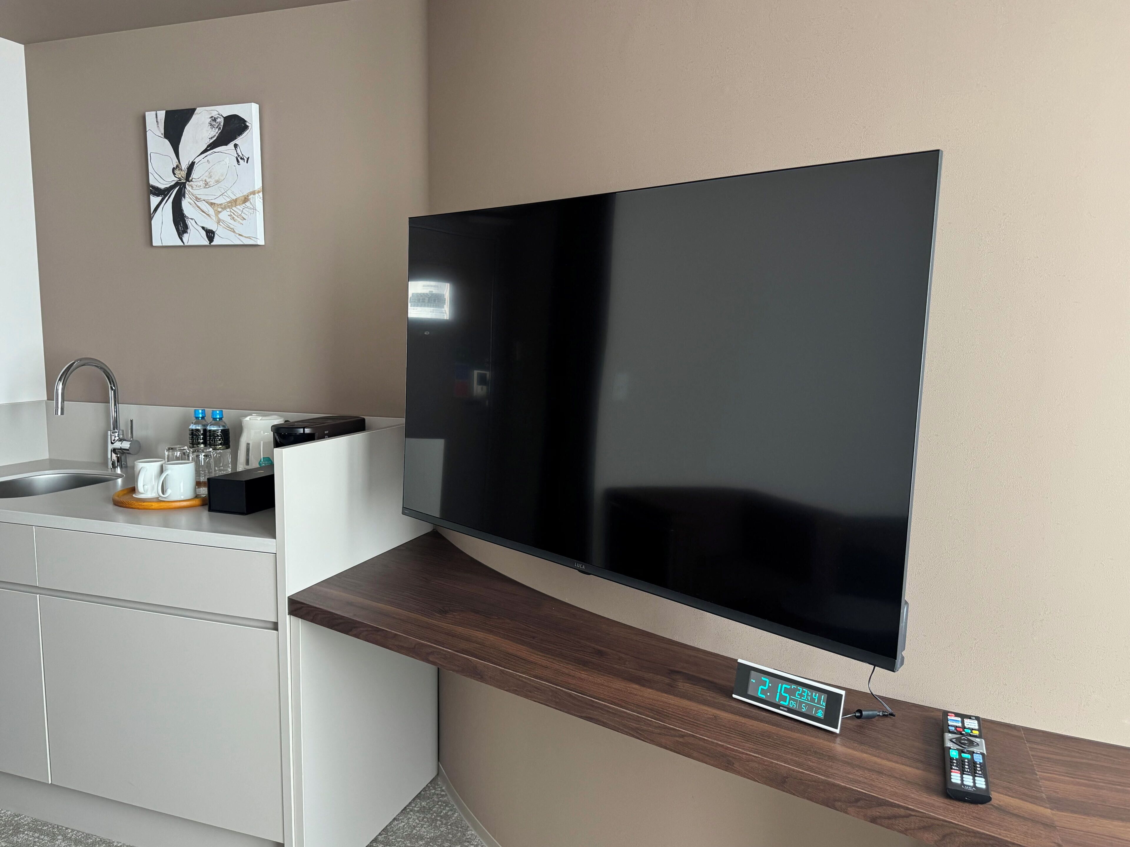 A modern kitchen with a flat-screen TV mounted on a wooden counter, a digital clock, and a remote control.