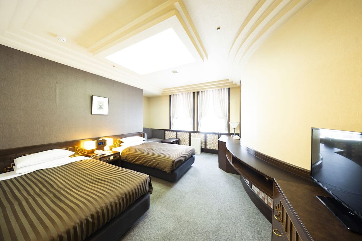 Une chambre d’hôtel avec deux lits, une télévision, un bureau et une fenêtre avec des rideaux.