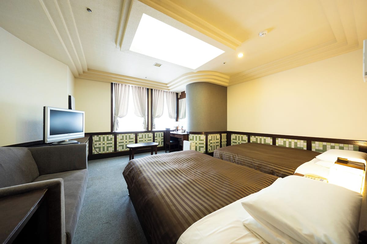 Une chambre d’hôtel avec un lit, une télévision, un bureau et une fenêtre avec des rideaux.