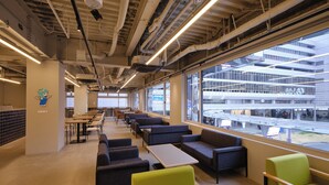 A modern interior with seating, tables, and large windows overlooking a building.