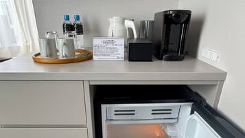 Et tekøkken med et køleskab fyldt med drikkevarer, en kaffemaskine og en bakke med kopper.