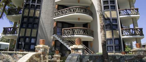 A multi-story hotel with balconies, stone staircases, and a tropical setting.