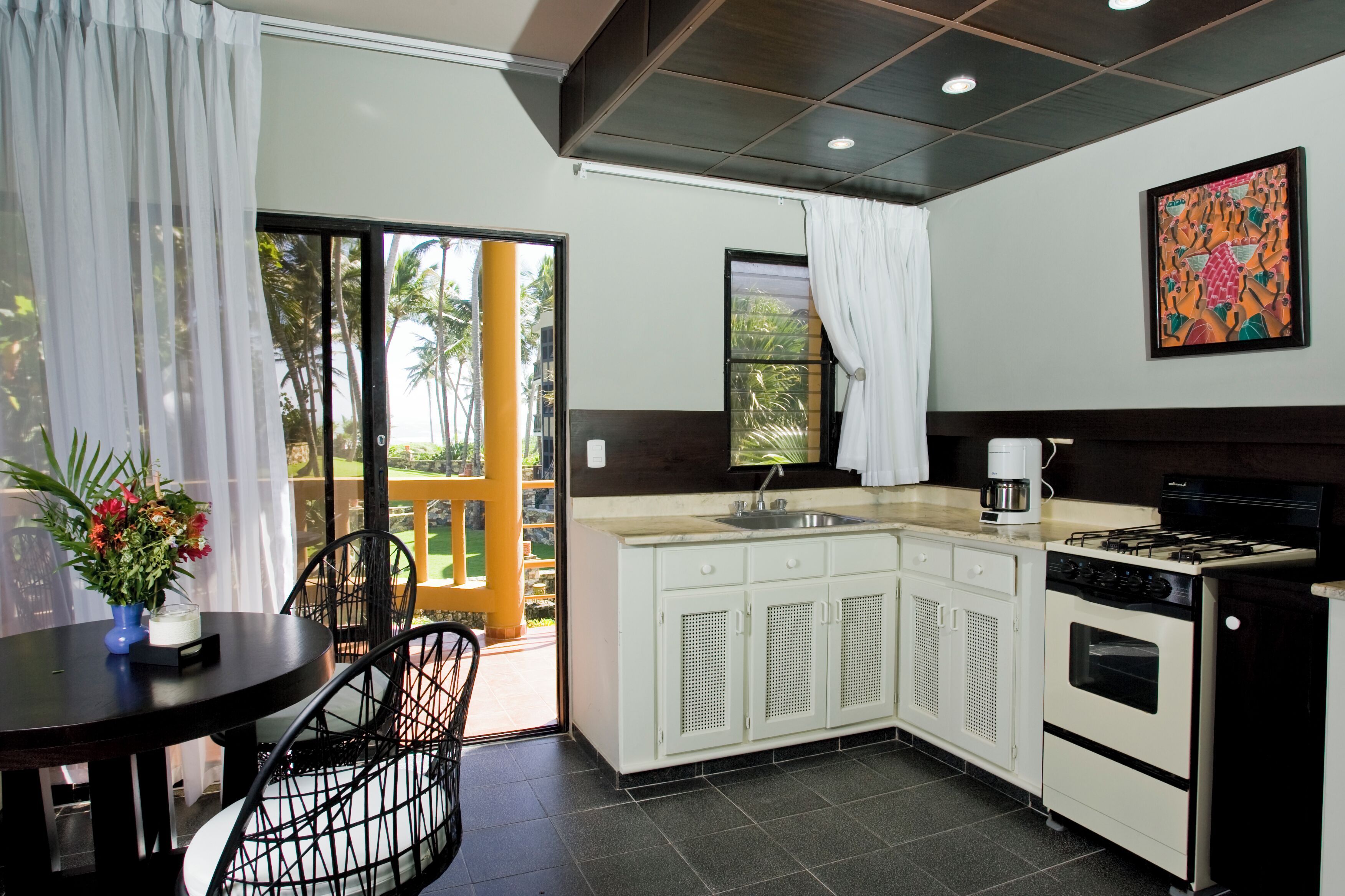A compact kitchen with a sink, stove, and cabinets. There is a dining area with a table and chairs.