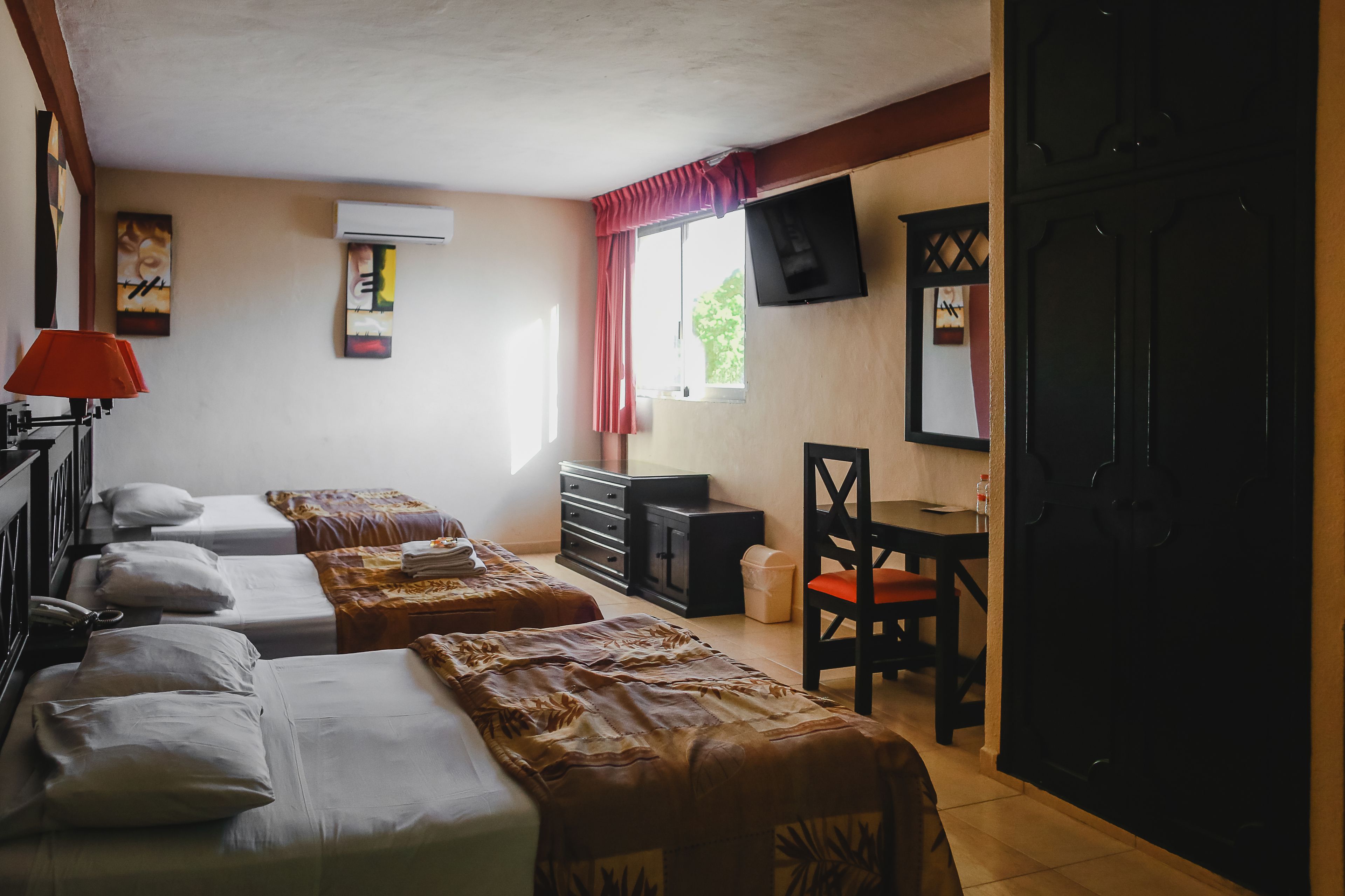 A hotel room with two beds, a desk, a chair, a TV, and a window with curtains.