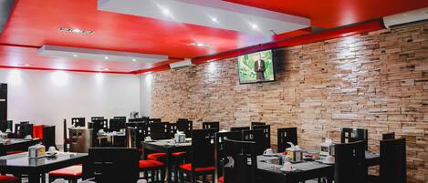 A restaurant with brick walls, red ceiling accents, and multiple tables with chairs.