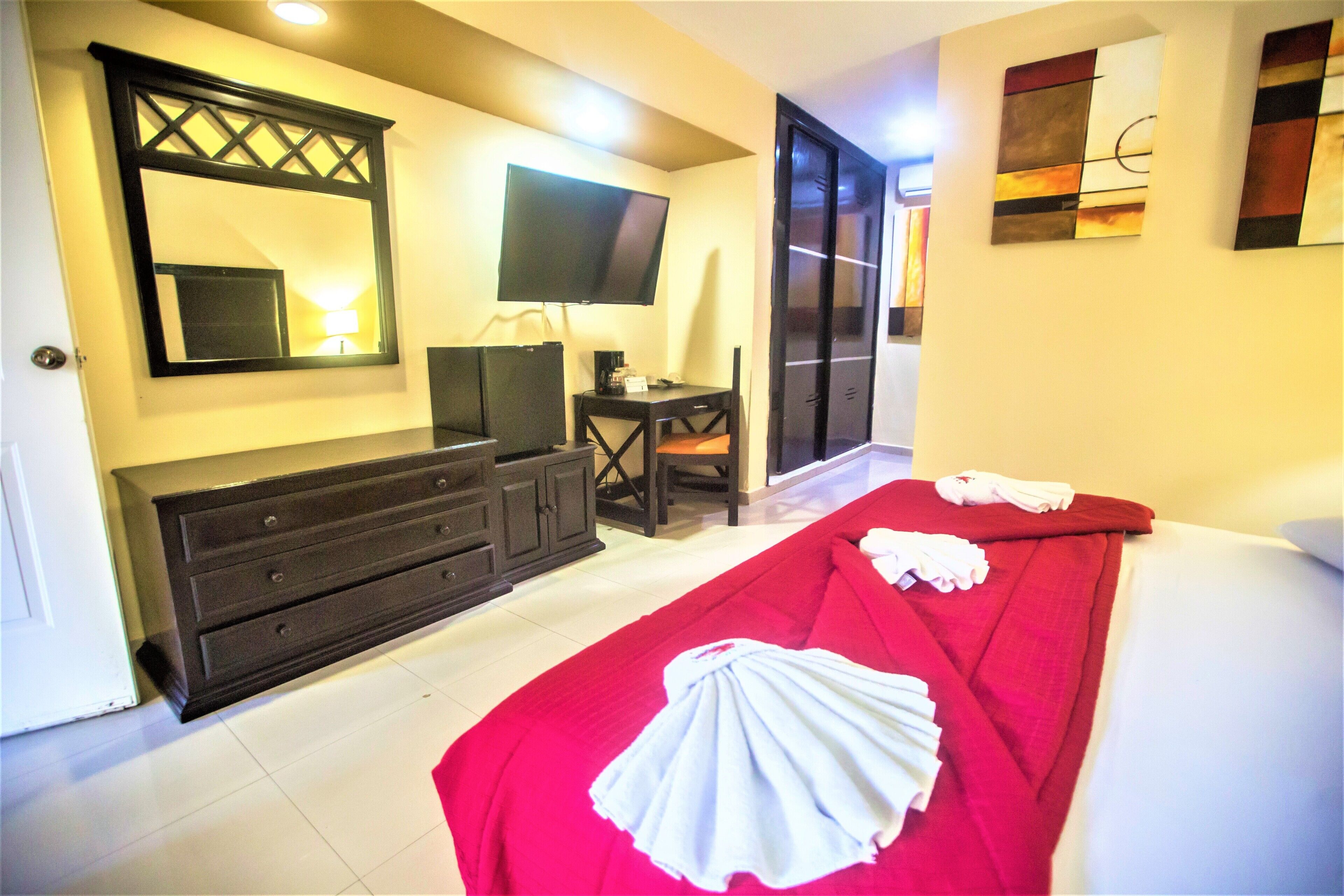 A hotel room with a bed, a desk, a chair, a television, and a wardrobe.