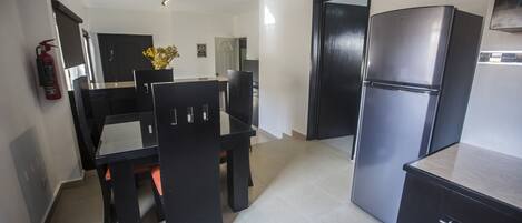 A compact kitchen with a dining table, chairs, a refrigerator, and a fire extinguisher.