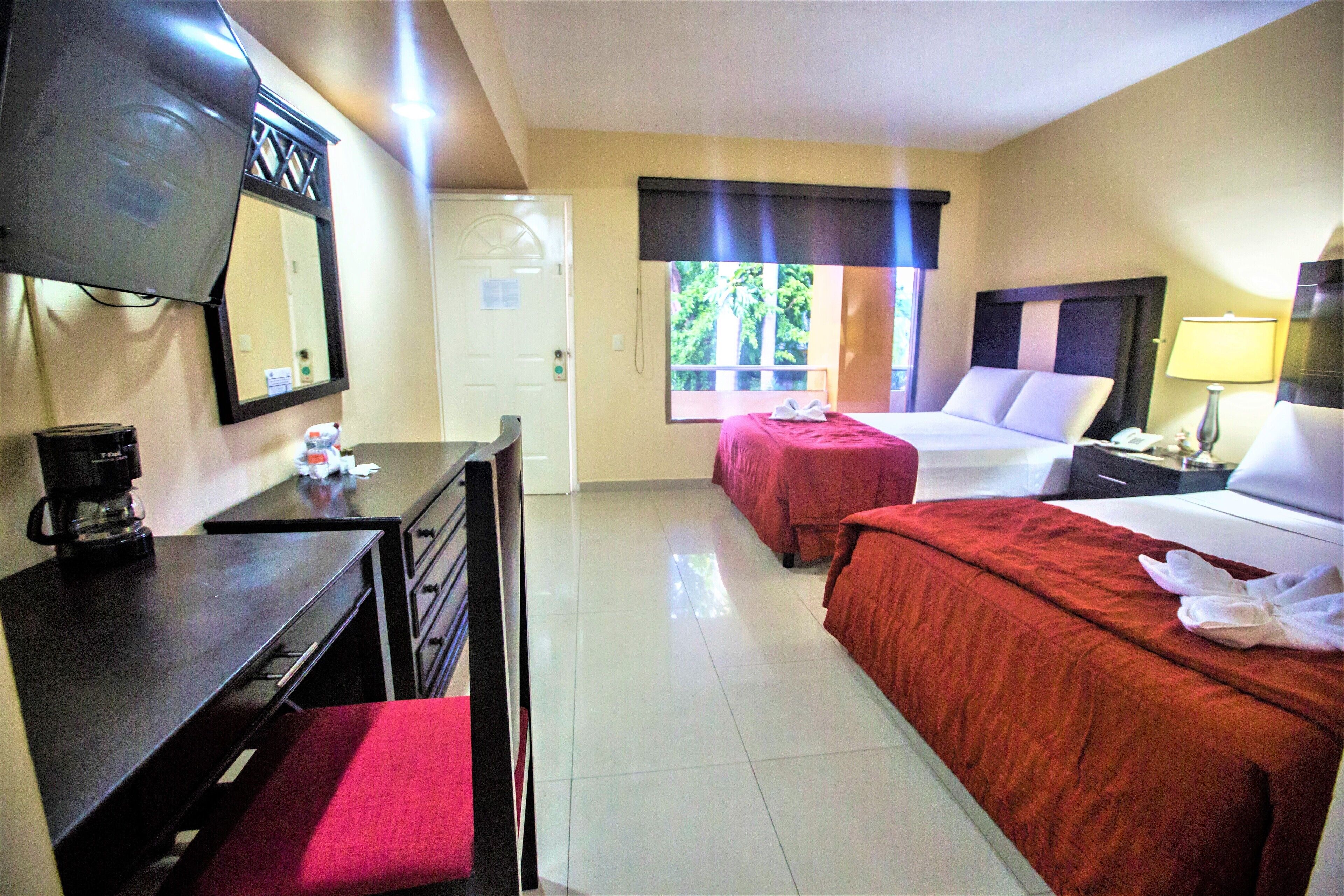 Habitación de hotel con dos camas, un escritorio, una silla, un televisor y una ventana con vista a árboles.