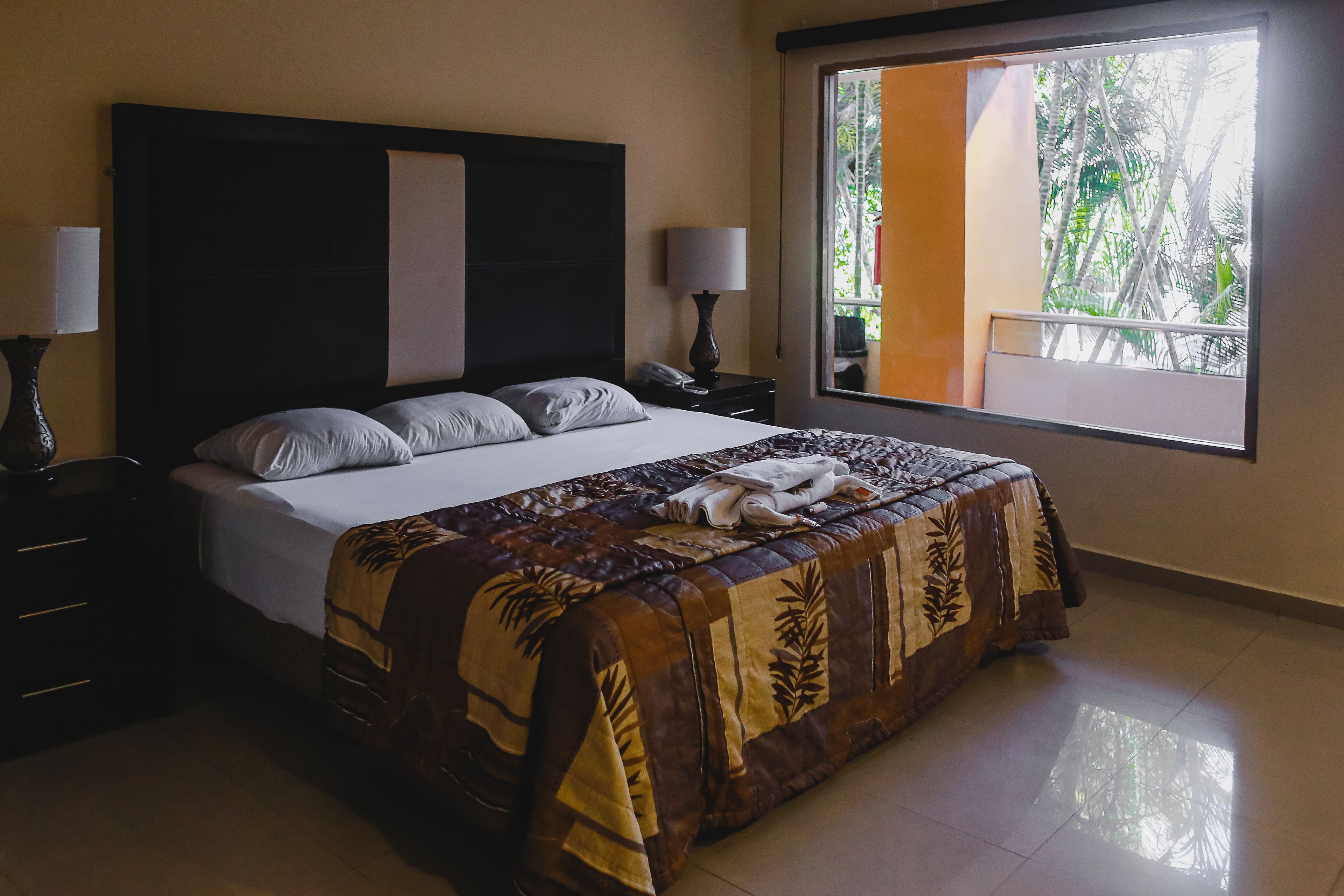 Un dormitorio con una cama grande, dos mesitas de noche y una ventana que da a zonas verdes.