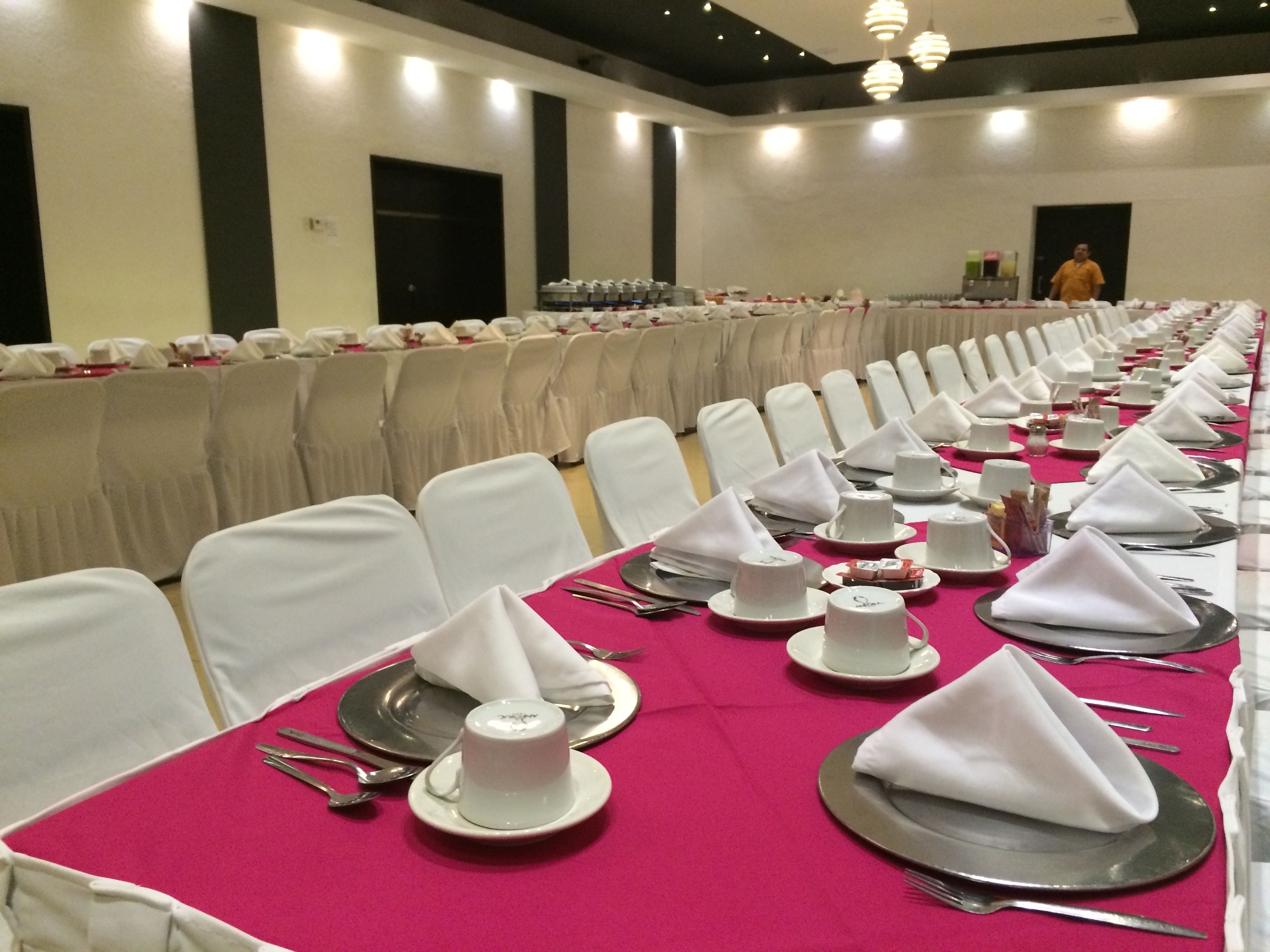 A banquet hall with rows of tables set for a formal event, complete with white napkins, plates, and cutlery.