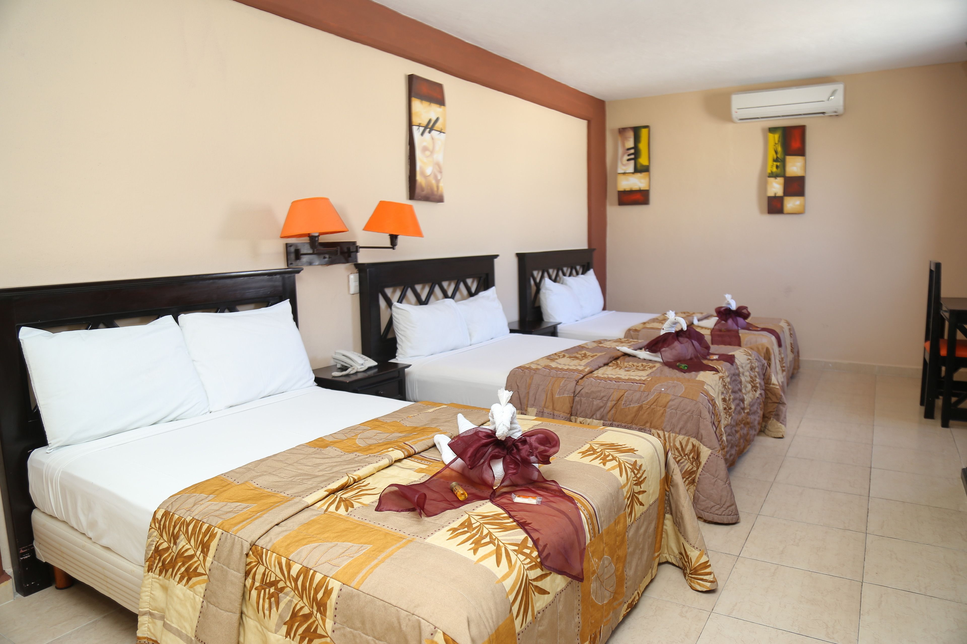 Habitación de hotel con tres camas, cada una con un edredón de diseño diferente. Hay dos lámparas de pared, un cuadro y un equipo de aire acondicionado.
