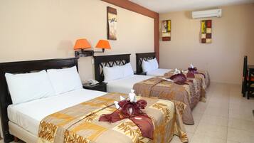 Habitación de hotel con tres camas, cada una con un edredón de diseño diferente. Hay dos lámparas de pared, un cuadro y un equipo de aire acondicionado.