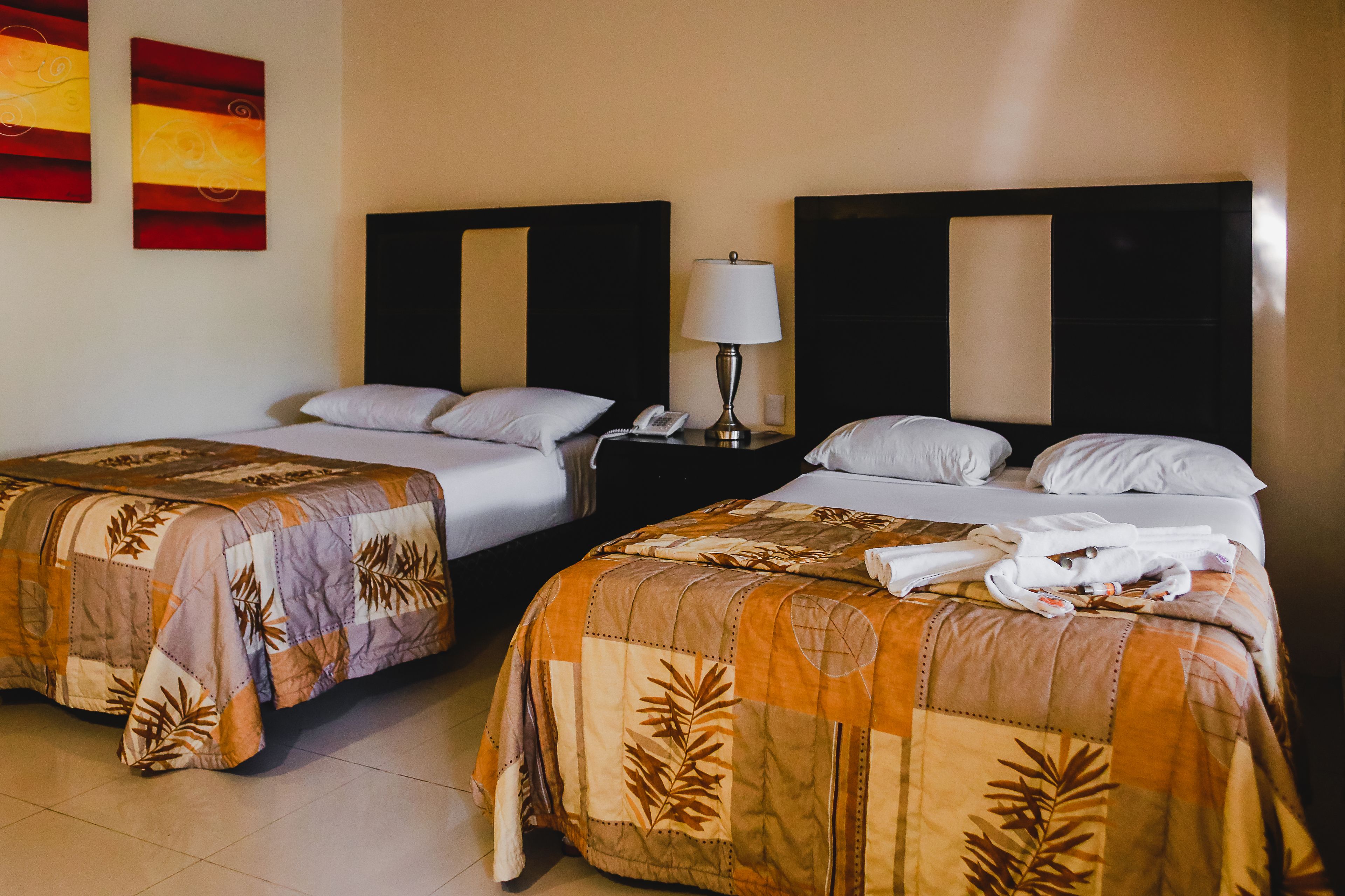 A hotel room with two beds, each with a floral-patterned bedspread, a nightstand with a lamp, and a telephone.