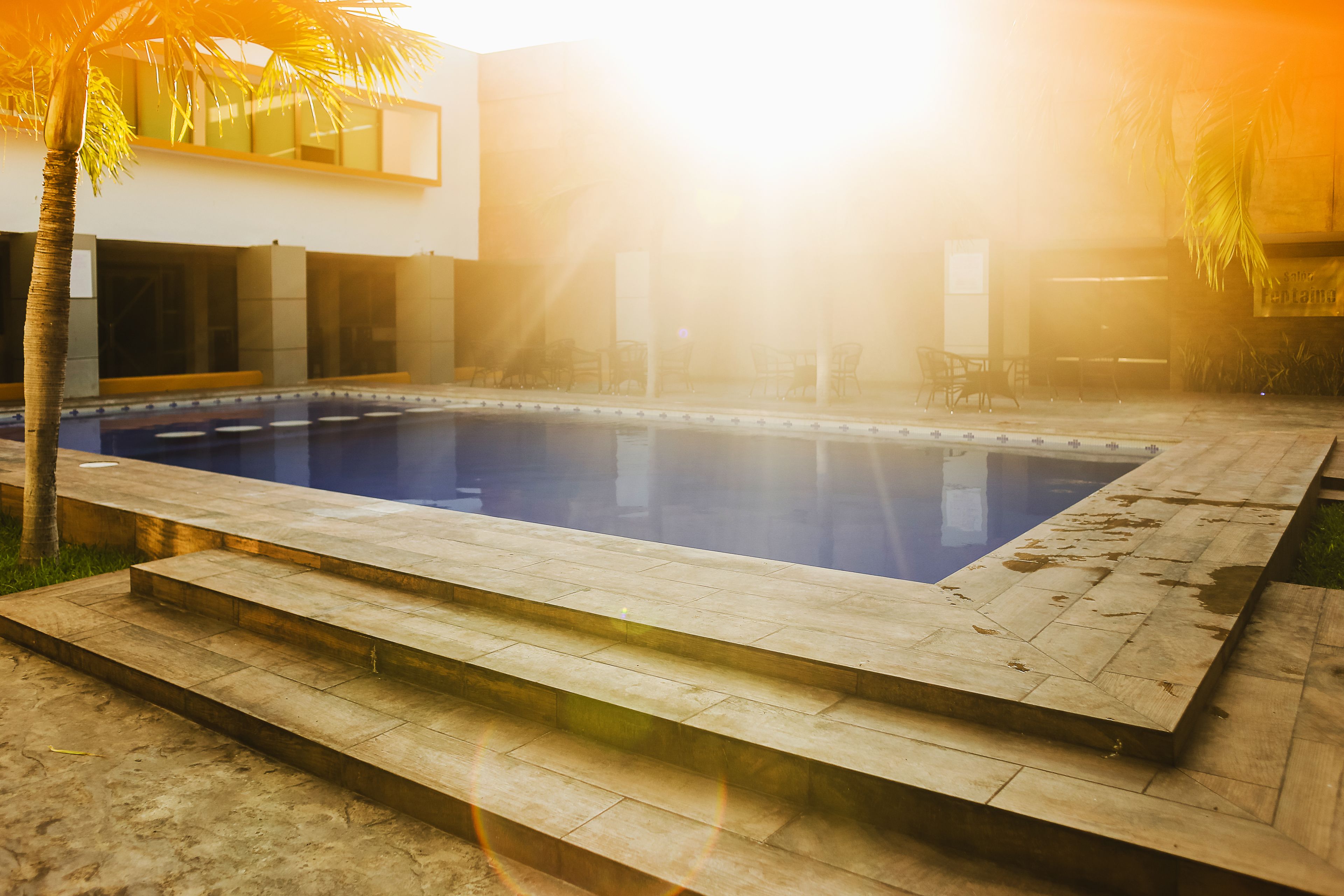 A swimming pool with steps leading into it, surrounded by a modern building and palm trees.