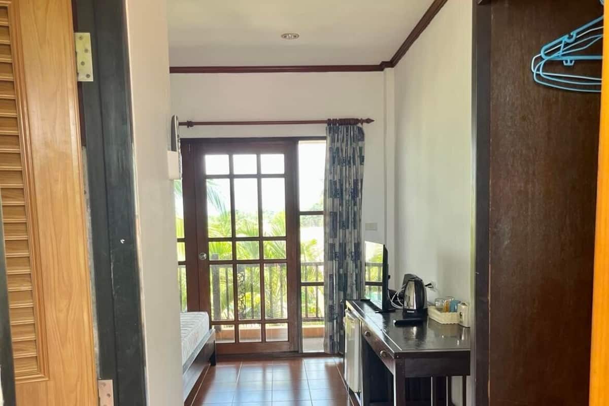 A room with a large sliding glass door leading to a balcony, a small kitchenette with a coffee maker, and a wooden door on the right.