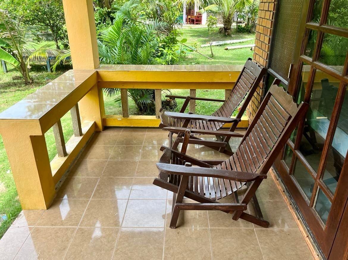 A covered outdoor seating area with two wooden chairs and a yellow railing.