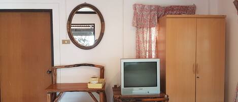 Une chambre avec une armoire en bois, un téléviseur posé sur un meuble en bois, un miroir et un climatiseur fixé au mur.