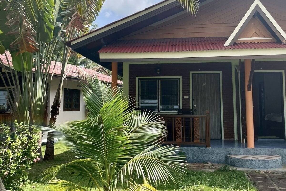 A two-story house with a red-tiled roof, a covered porch, and a well-maintained lawn with palm trees.