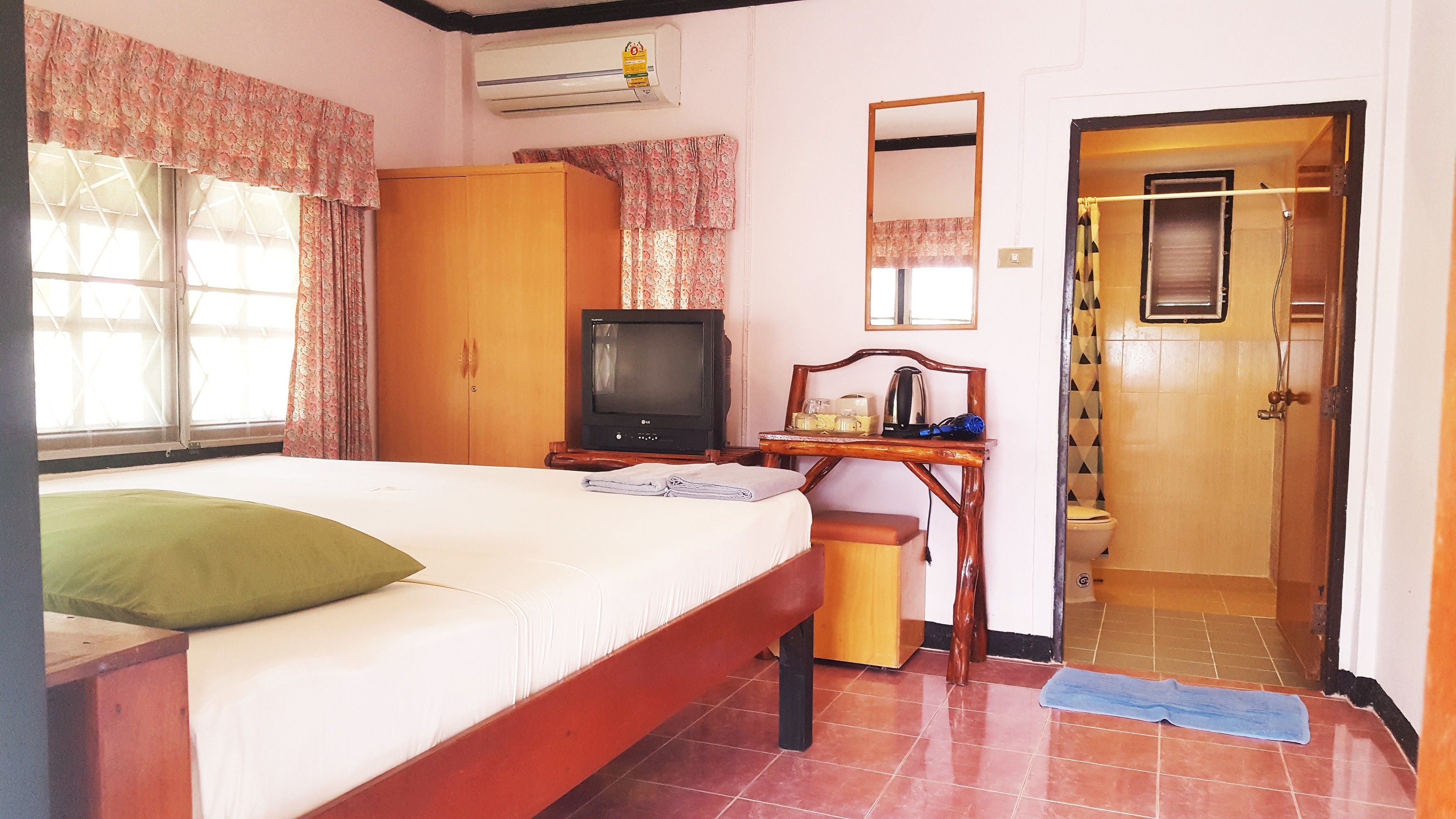 Un dormitorio con cama, televisión, armario, espejo y baño visible a través de una puerta abierta.