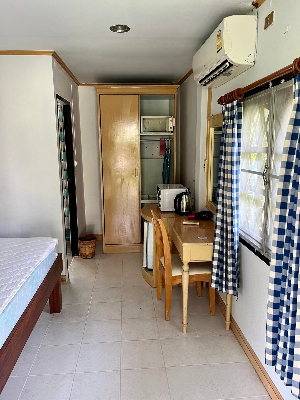 A compact room with a bed, a small table with chairs, a microwave, and a window with checkered curtains.