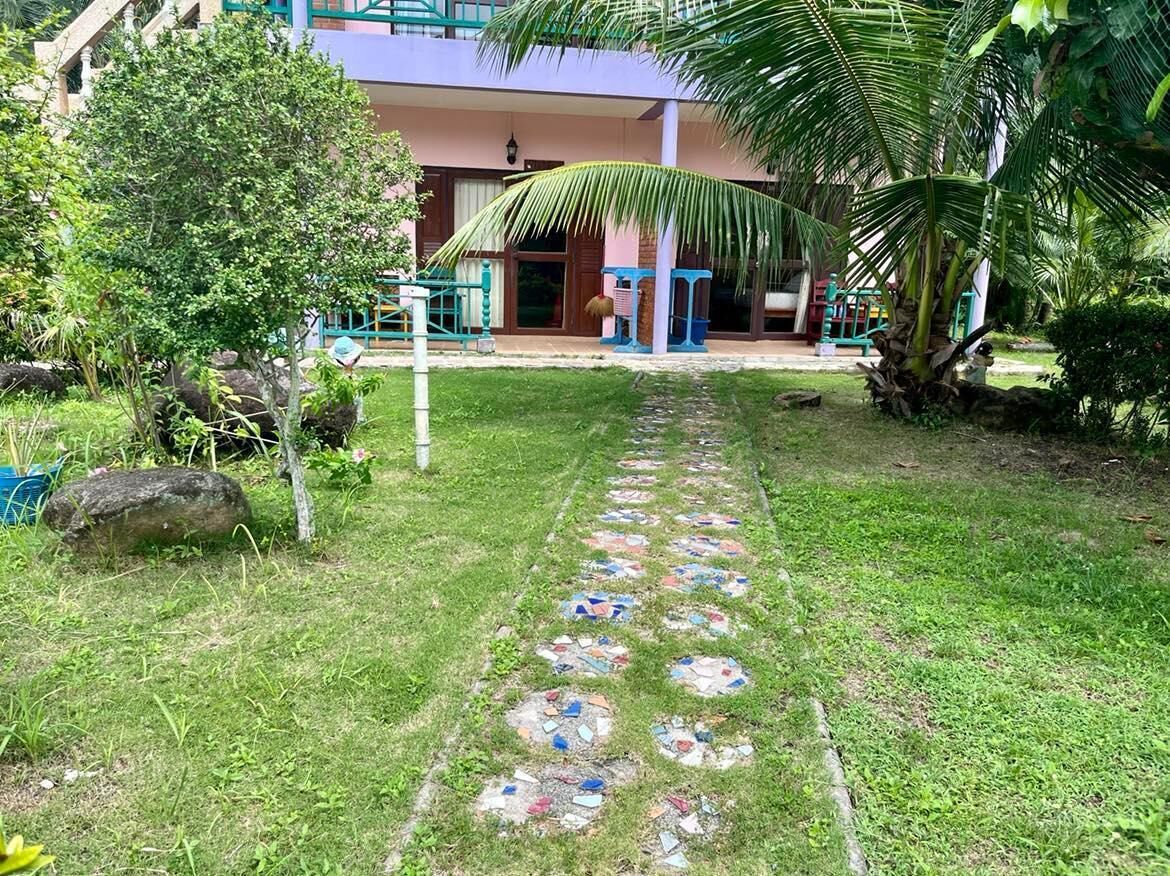 A pathway with colorful mosaic tiles leading to a building with a porch and a palm tree.