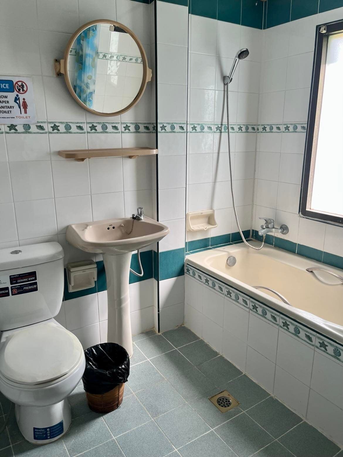Un baño con inodoro, lavamanos y bañera. Hay un espejo sobre el lavamanos y un cabezal de ducha sobre la bañera. Las paredes están revestidas con un diseño azul y blanco.