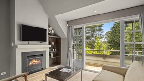 Een moderne woonkamer met een open haard, een flatscreen televisie, een bank en een groot raam met uitzicht op een balkon.