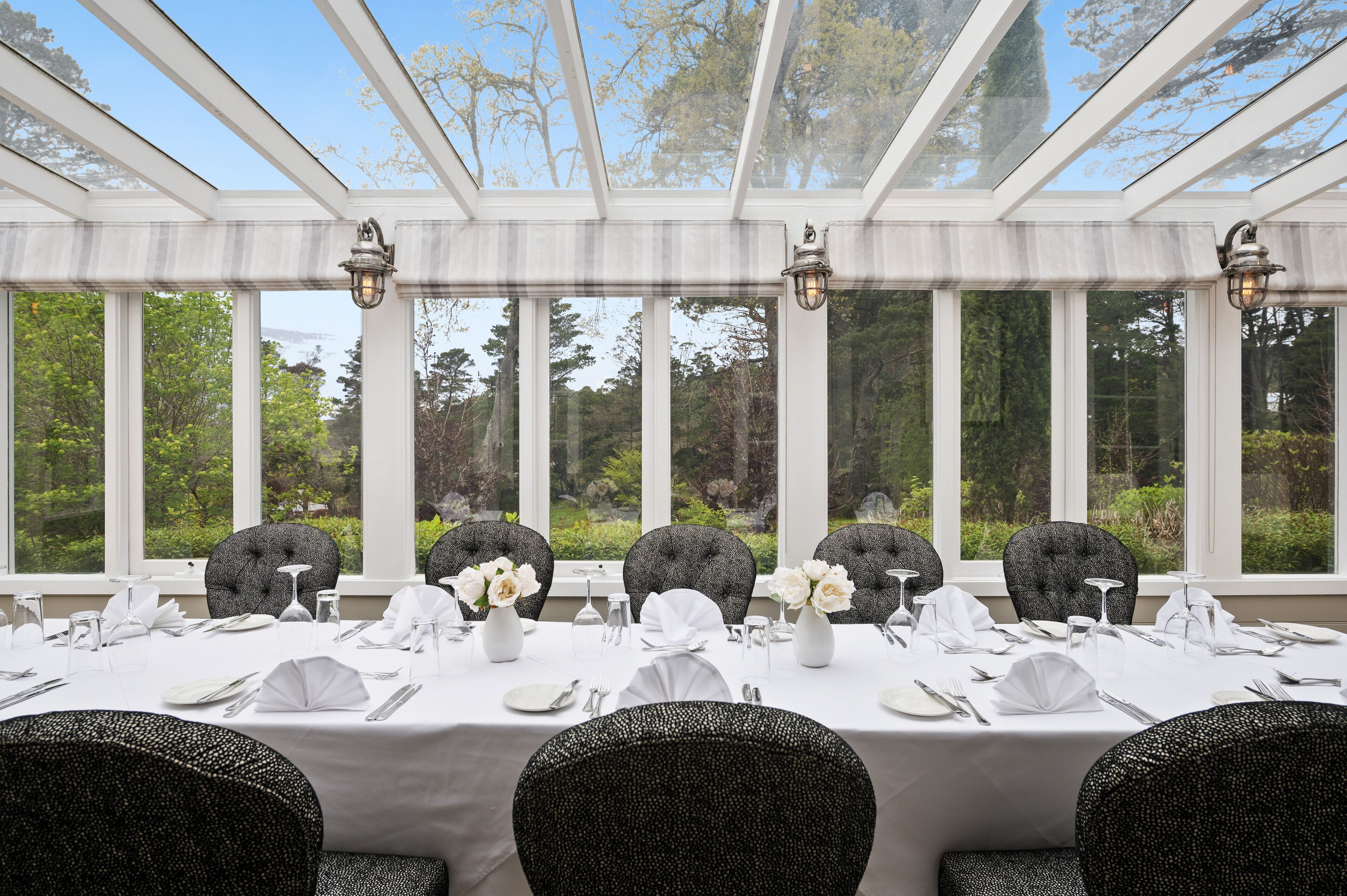A conservatory dining area with a table set for six, large windows, and a view of greenery.