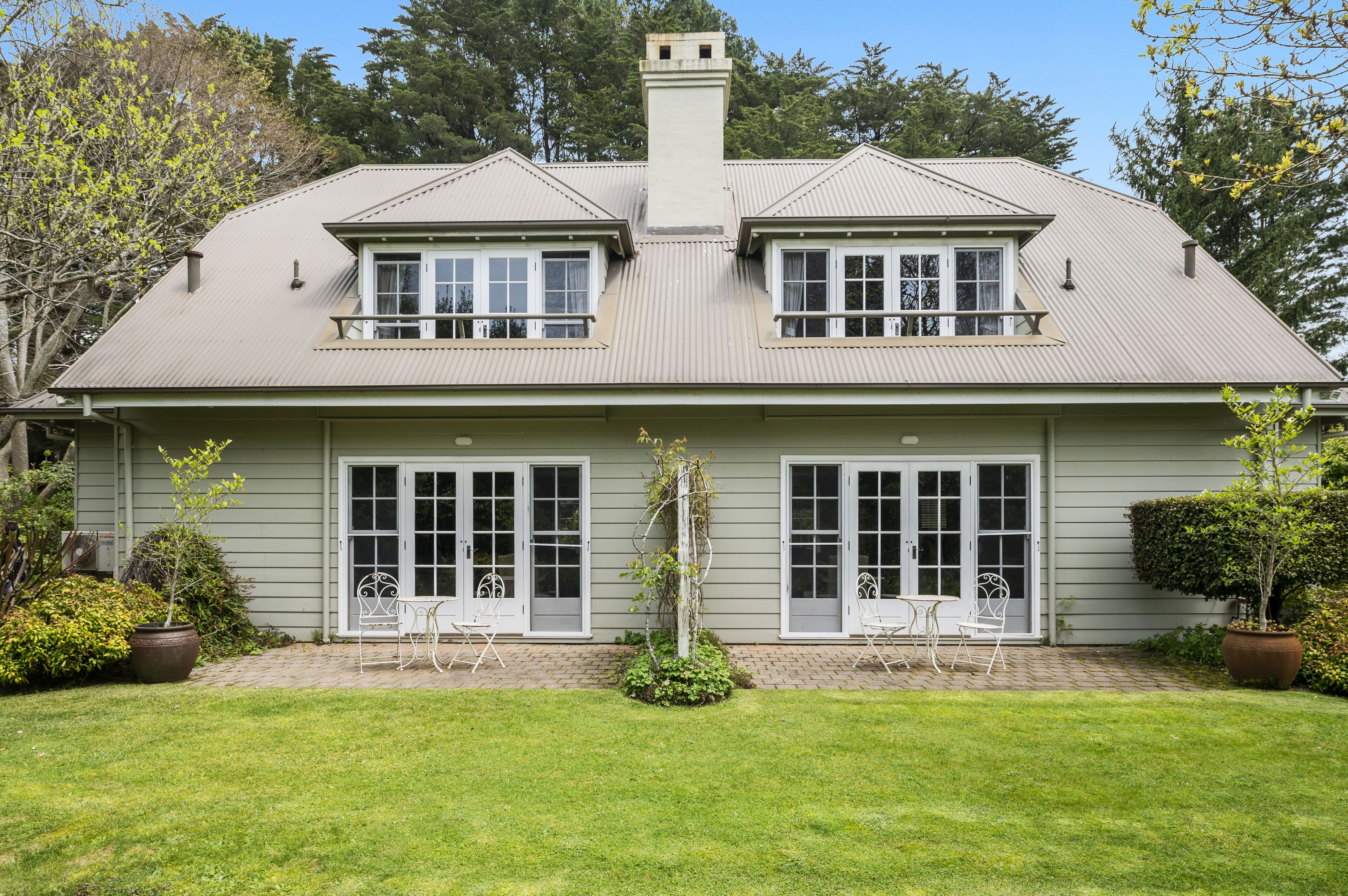 Una casa de dos pisos con fachada simétrica, ventanas grandes y un patio cubierto con mobiliario exterior.