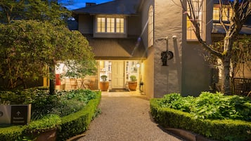 A well-lit reception area with a gravel path leading to the entrance, surrounded by neatly trimmed hedges and potted plants.