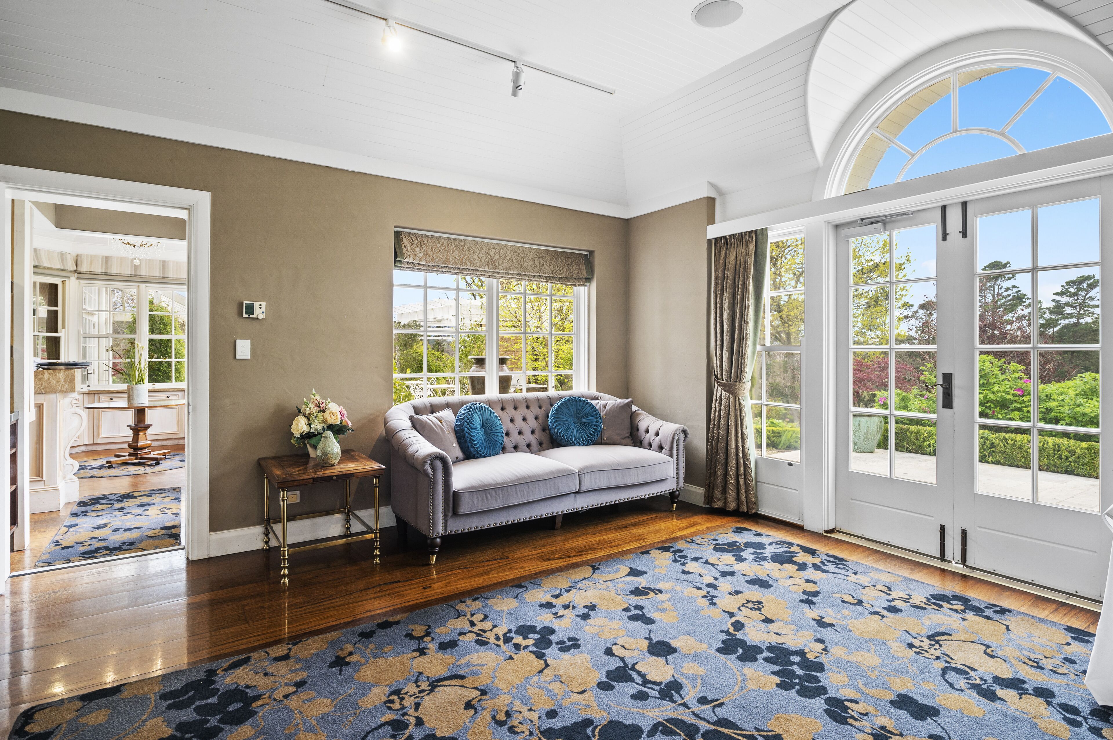 A spacious room with a large window, a grey sofa, and a patterned rug.