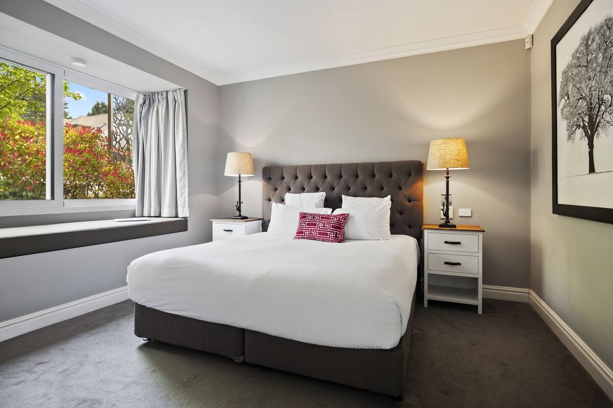 A bedroom with a large bed, two bedside tables, and a window with curtains.